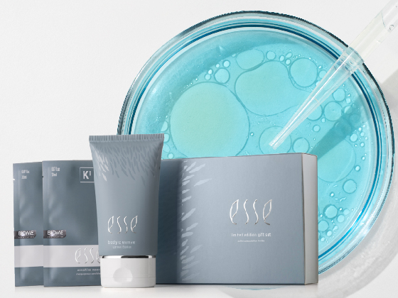 Blog Images Swap-05 Skincare products including a tube and packets labeled "ESSE" are displayed in front of a glass dish filled with blue liquid. A dropper is resting on the dish, suggesting a scientific or cosmetic theme. The products and dish are on a white background.