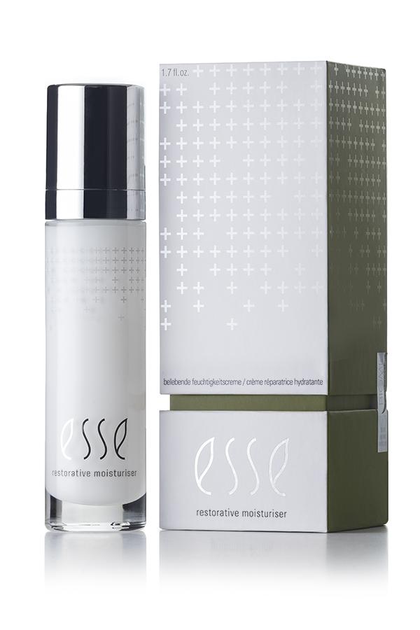 A product shot of Esse Restorative Moisturiser. The image features a white bottle with a silver cap placed beside its rectangular grey-and-green packaging. Both the bottle and the box display the Esse logo and product name in white text, complementing their minimalist design.