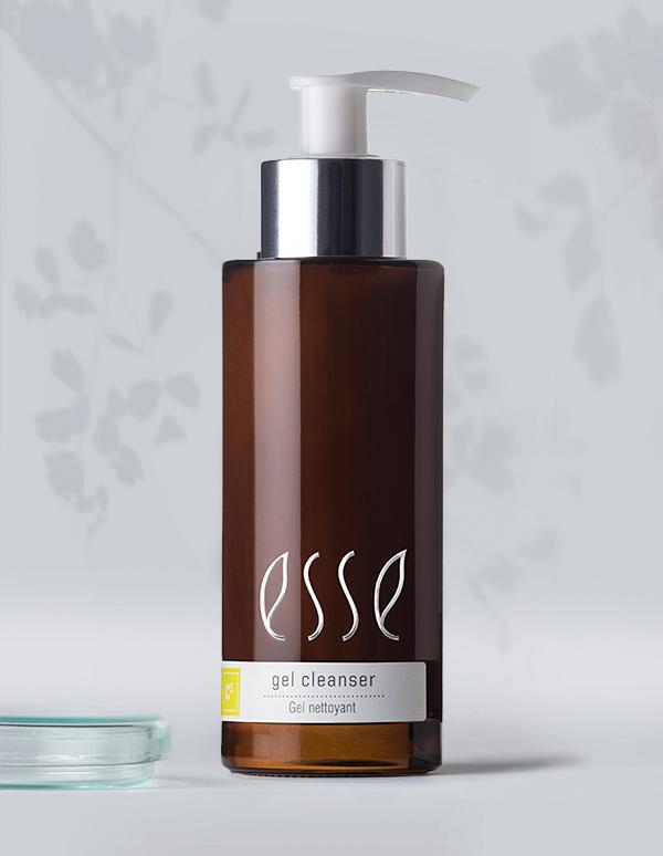 A brown bottle of Esse gel cleanser with a white pump dispenser. The label reads "gel cleanser" in white text and "Gel nettoyant" below it. The bottle is placed against a gray background with subtle leaf patterns.