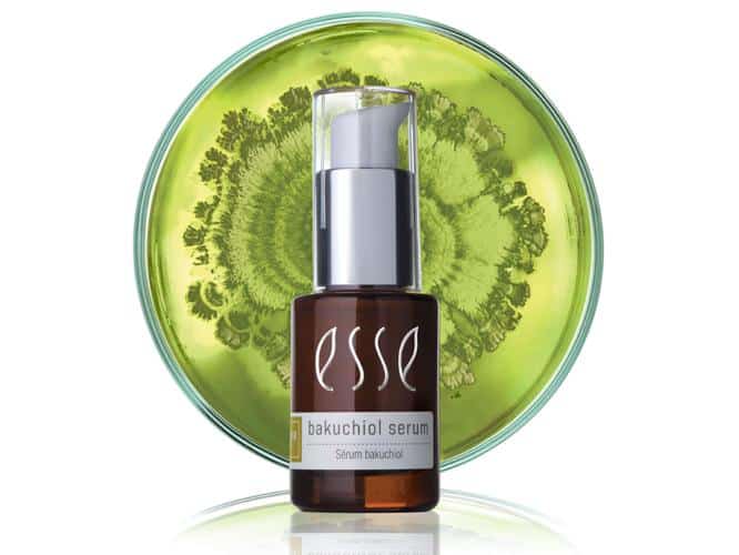 BAKUCHIOL_SERUM_Microbe-666-x-500px A bottle of Esse Bakuchiol Serum with a pump dispenser sits in front of a green background featuring a circular botanical design. The bottle is brown with a white label displaying the product name.